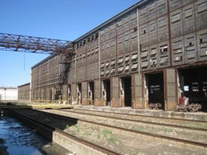 An image of an old and abandoned train station along the water, with a rusted walkway going across.